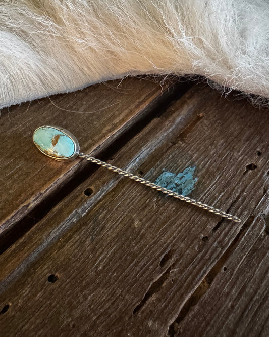 Teal stone hairpin on a wooden surface with fur