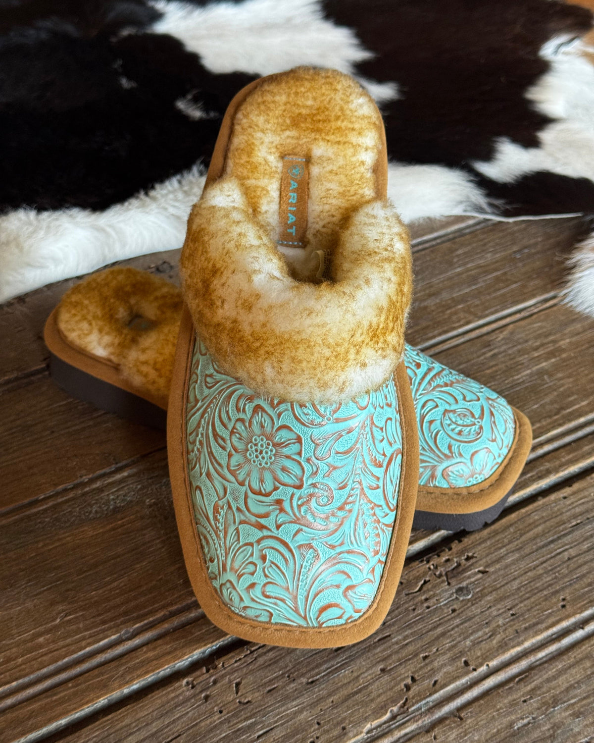 turquoise embossed leather slippers on a rustic wooden table with cowhide background