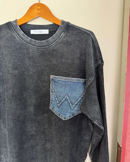Dark gray corduroy shirt with a patch on a hanger against a beige background