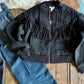 Black fringed jacket on a wooden surface with jeans and cowhide rug