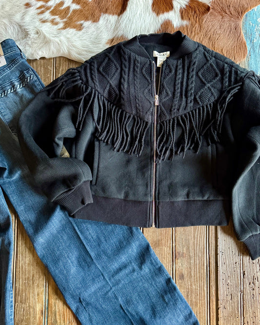 Black fringed jacket on a wooden surface with jeans and cowhide rug