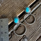 Silver earrings with turquoise stones on a wooden surface next to a ruler for scale.