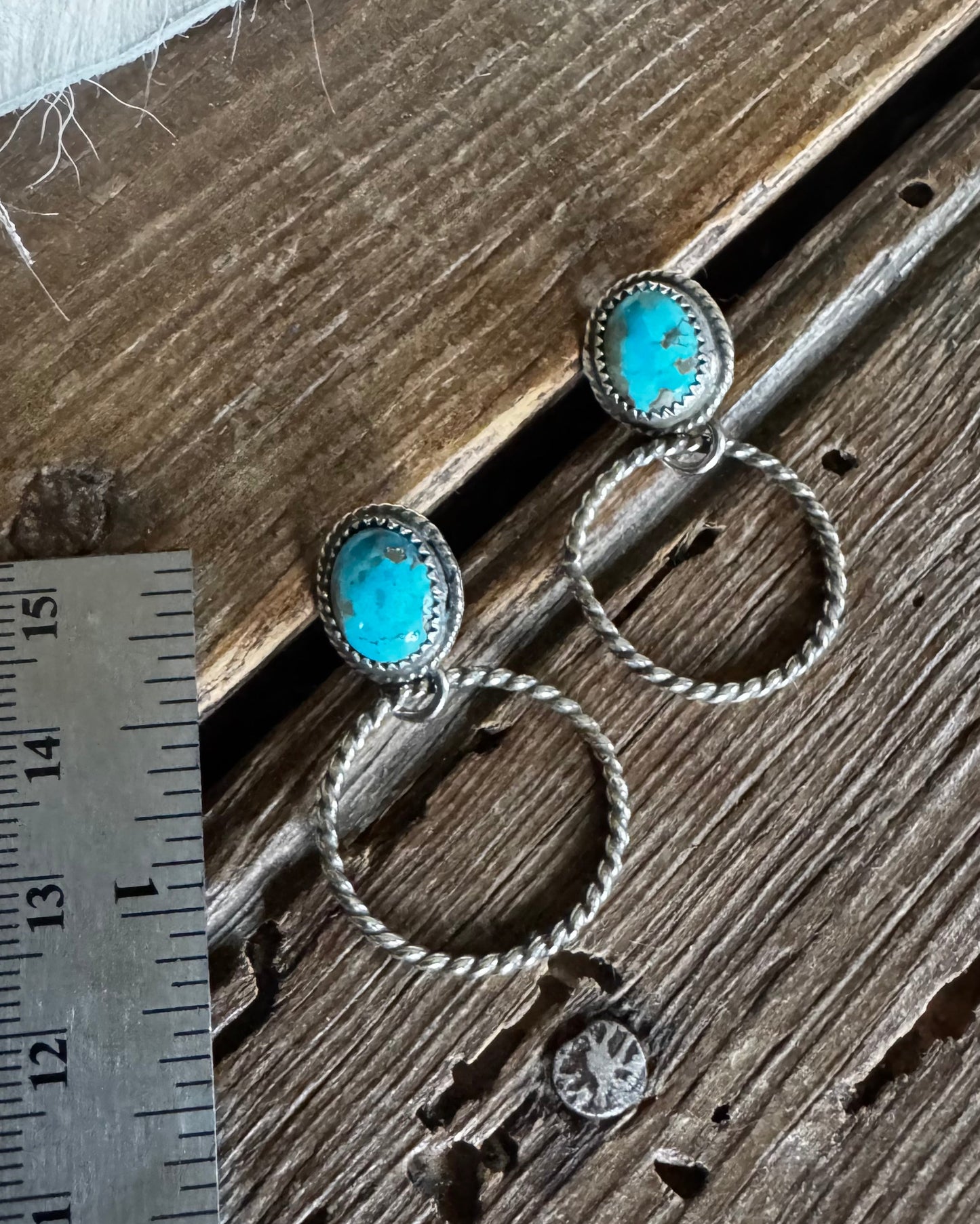 Silver earrings with turquoise stones on a wooden surface next to a ruler for scale.
