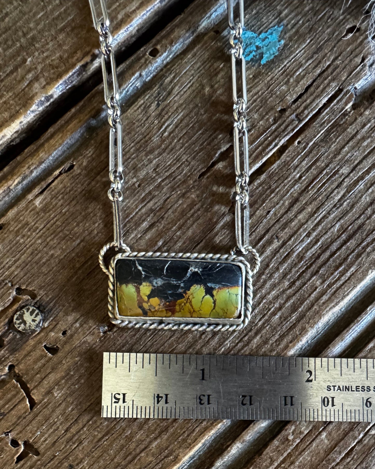 Necklace with a pendant on a wooden surface, measured by a ruler.
