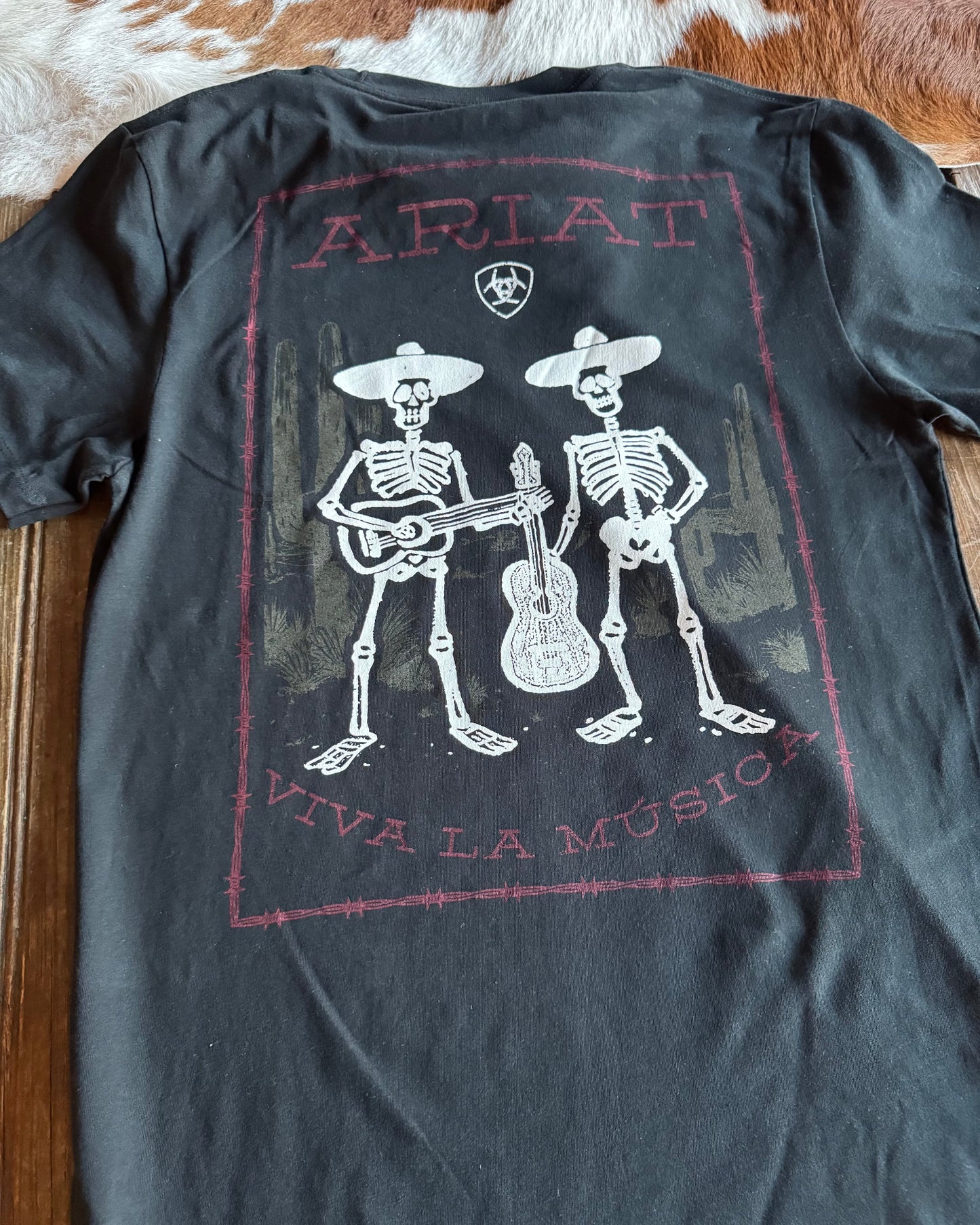 Black t-shirt with skeleton design and 'Ariat' branding on a wooden surface.