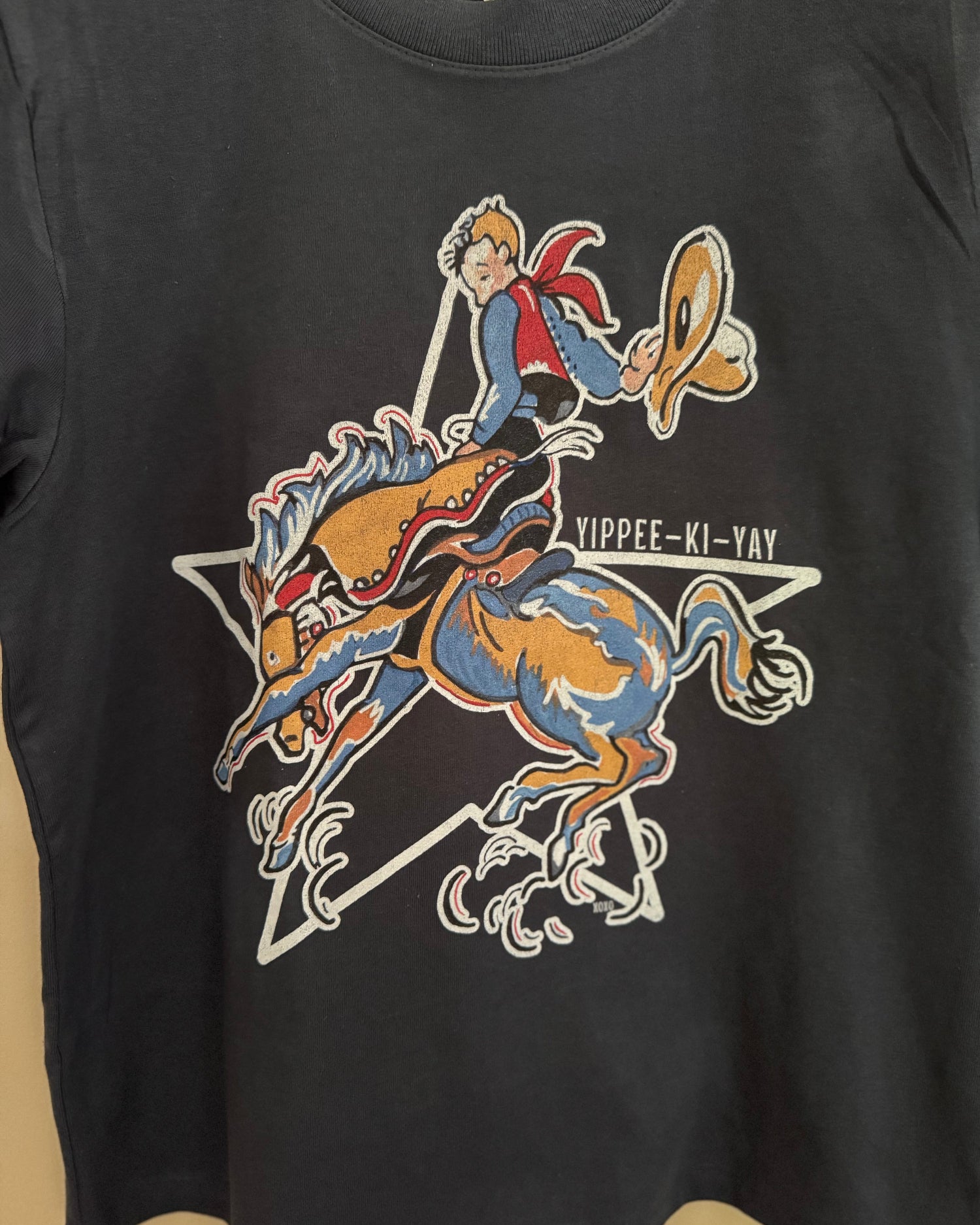 Black t-shirt with a colorful graphic of a cowboy riding a horse and the text 'Yippee Ki Yay' on a beige background.