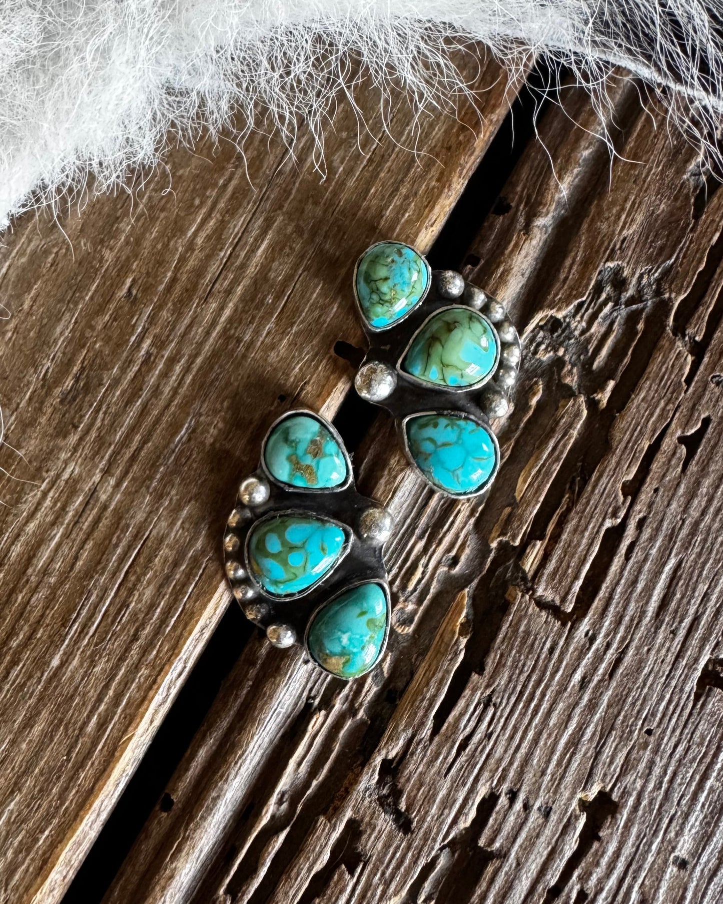 Turquoise earrings on a wooden surface with white fur