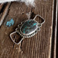 Silver pendant with a green stone on a wooden surface