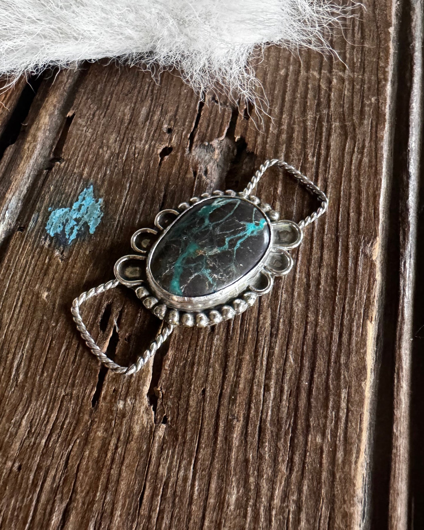 Silver pendant with a green stone on a wooden surface