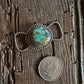 Silver twilly slide with turquoise stone next to a coin on wooden surface