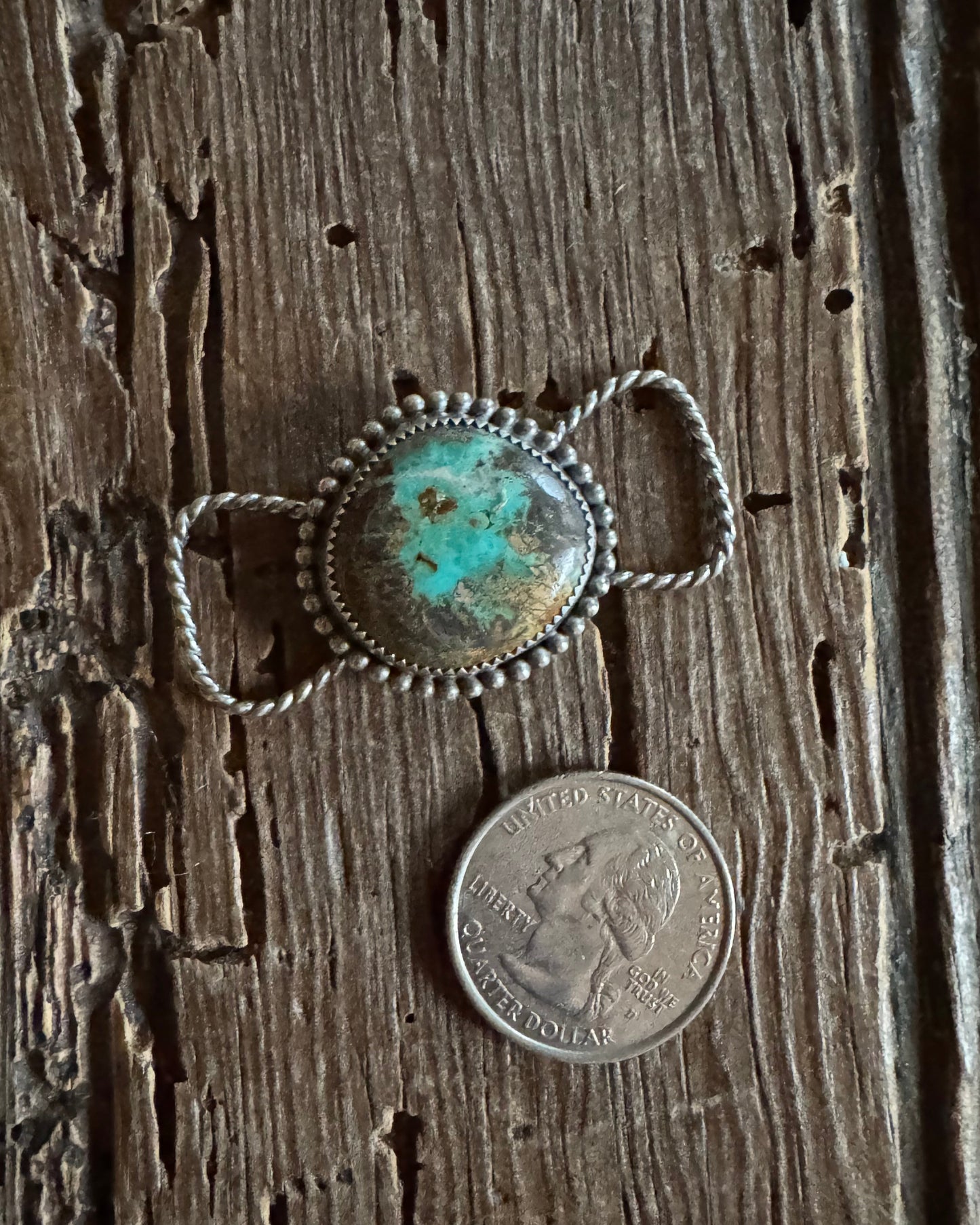 Silver twilly slide with turquoise stone next to a coin on wooden surface