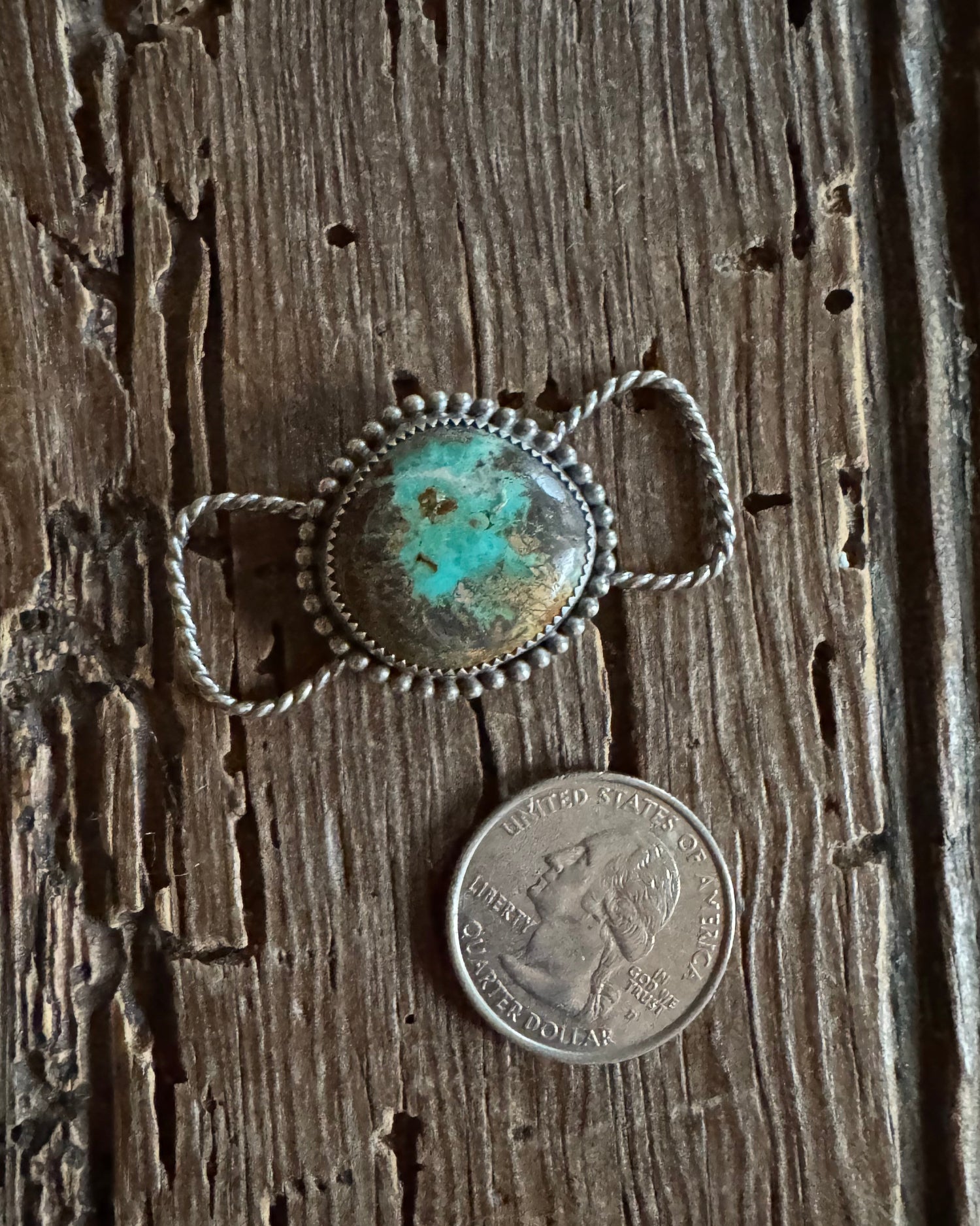 Silver twilly slide with turquoise stone next to a coin on wooden surface