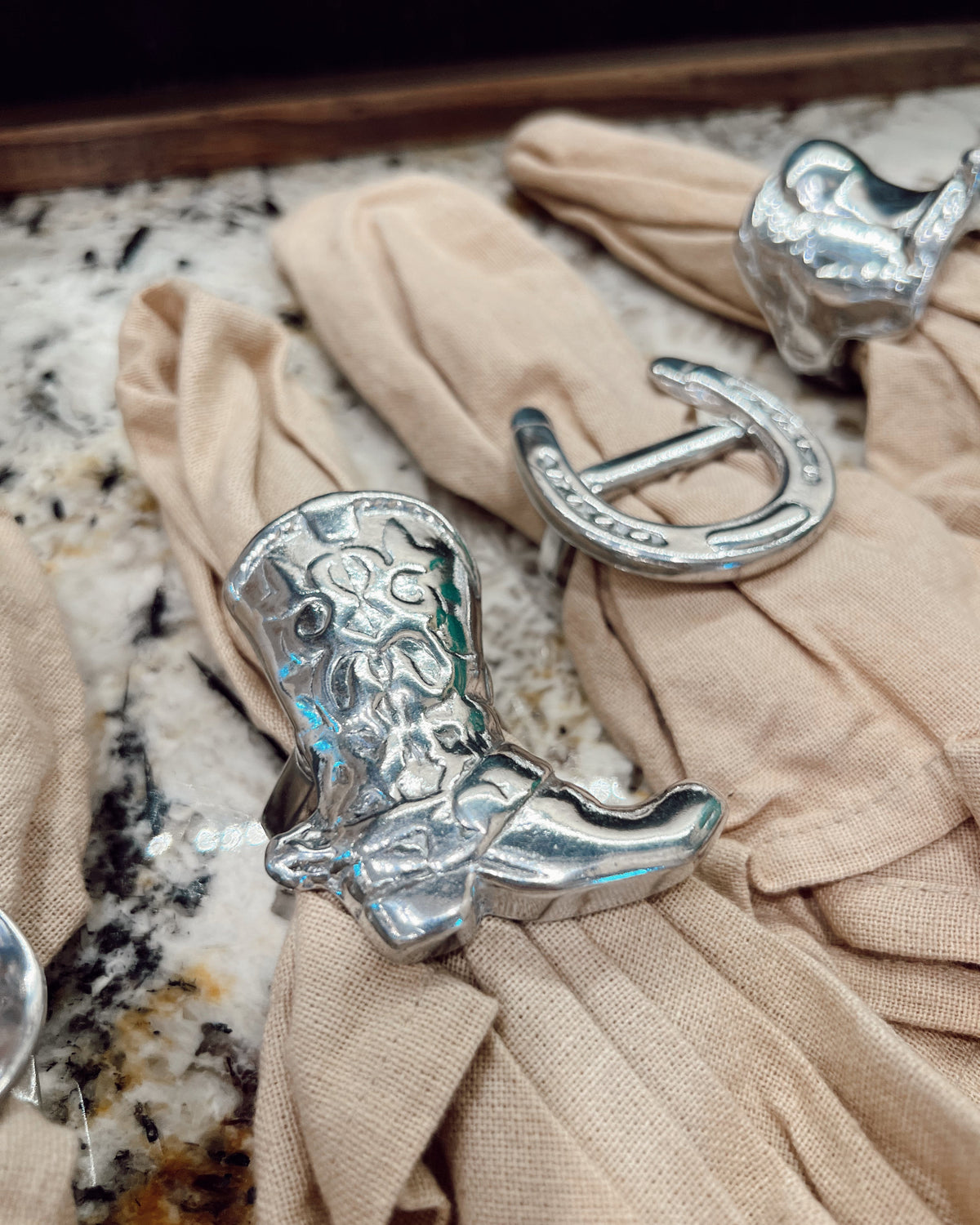 Silver cowboy boot and horseshoe napkin rings on beige fabric