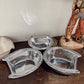 Three metal pet bowls on a wooden surface with a decorative item in the background.