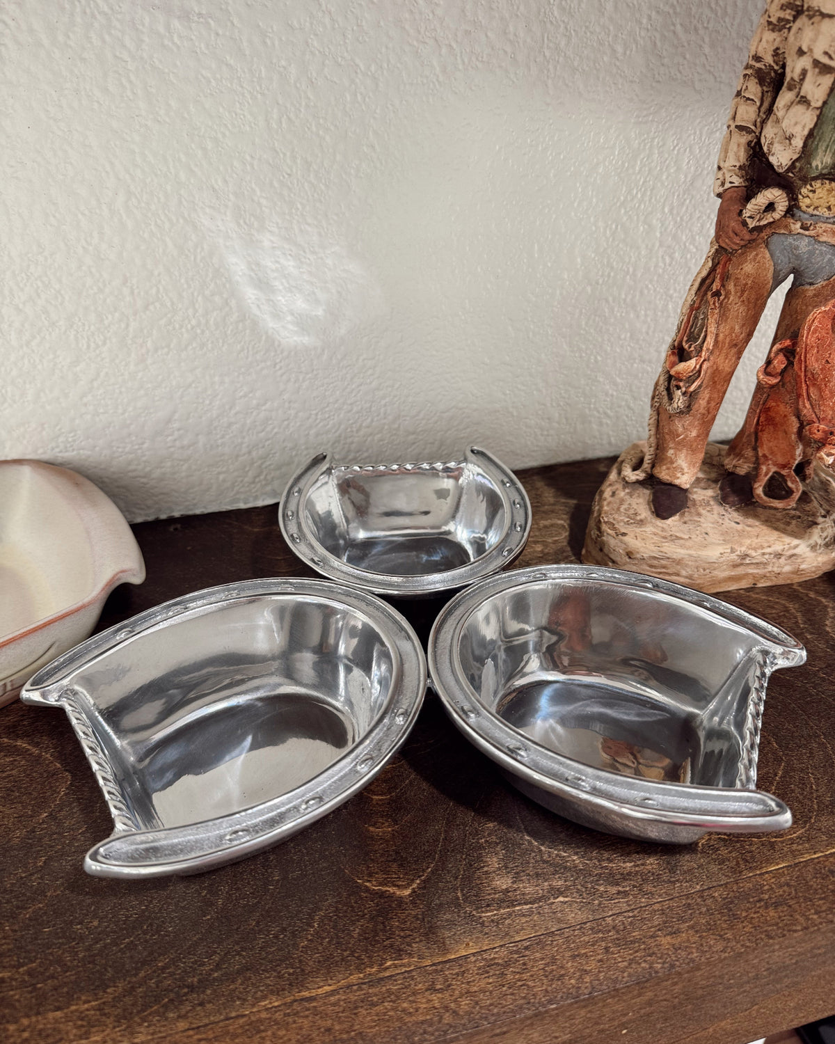 Three metal pet bowls on a wooden surface with a decorative item in the background.