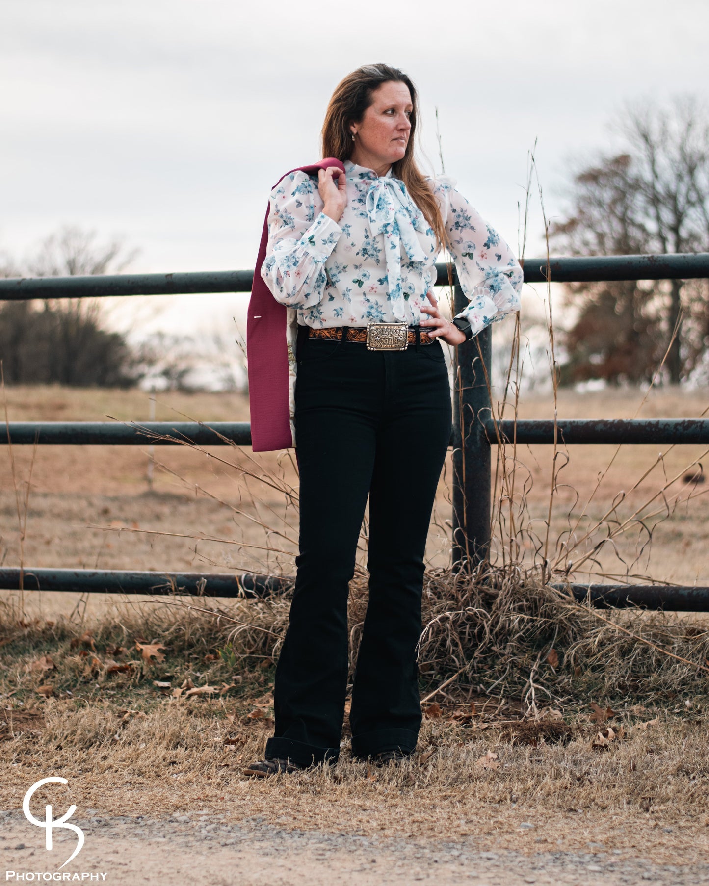 Model standing by a pipe fence in a field, dressed in a stylish modern western outfit.