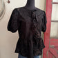 Black blouse with floral pattern on a mannequin against a neutral wall.