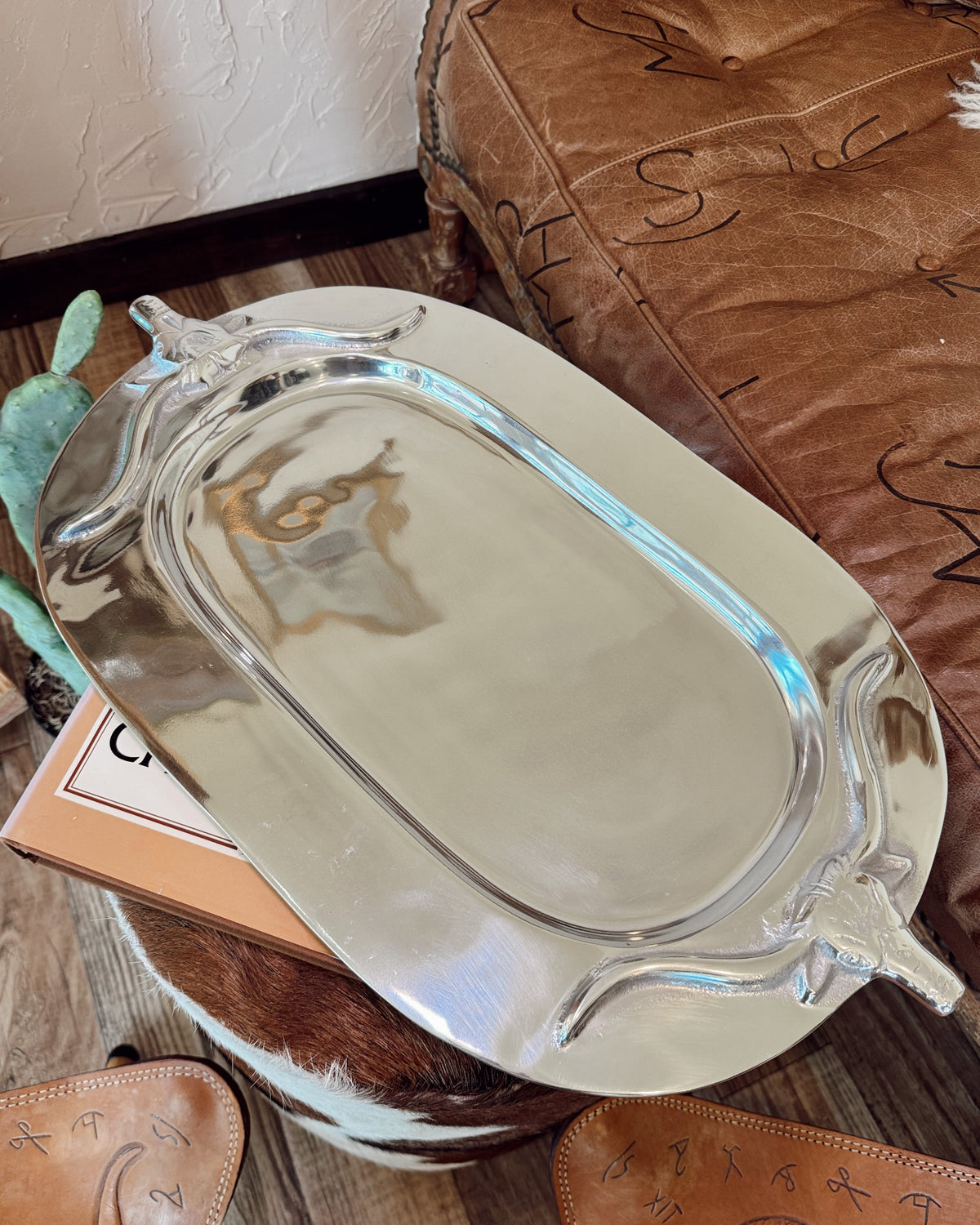 Silver tray on a wooden surface with a brown leather chair in the background