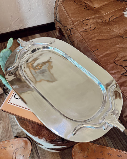 Silver tray on a wooden surface with a brown leather chair in the background