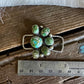 Green gemstone brooch on a wooden surface with a ruler for scale