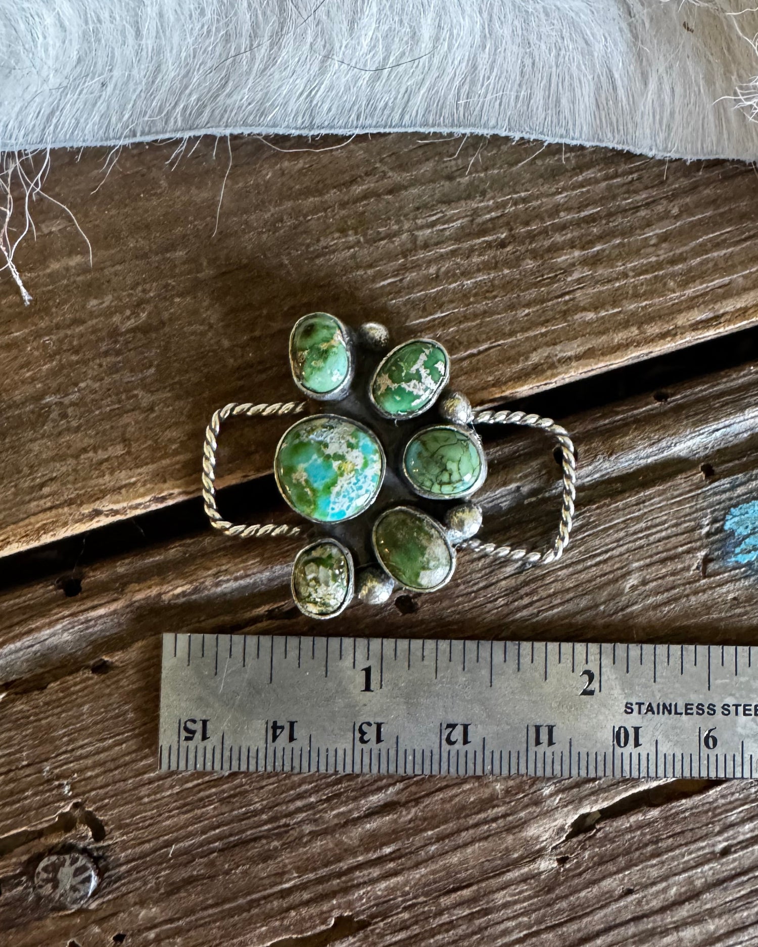 Green gemstone brooch on a wooden surface with a ruler for scale
