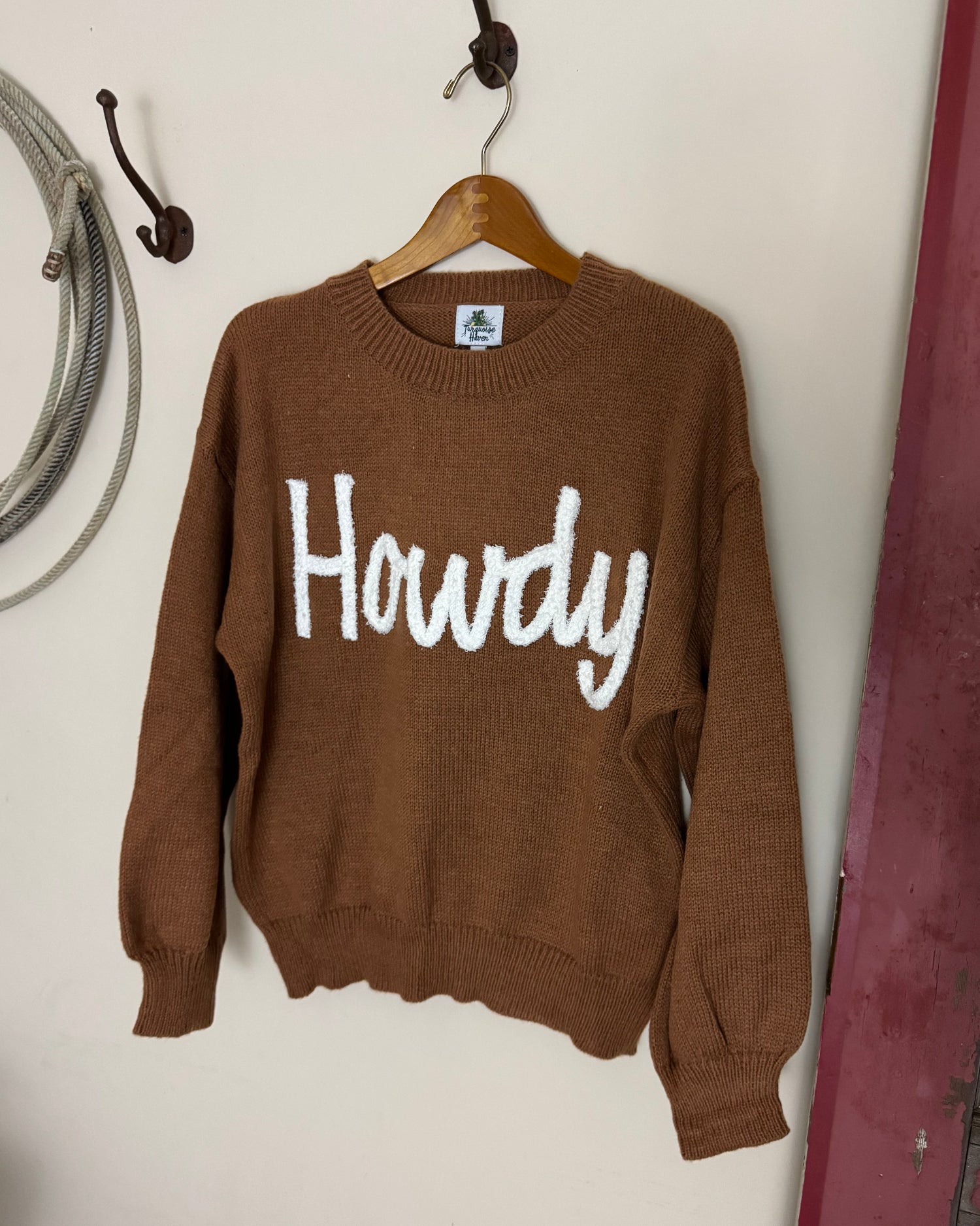 Brown sweater with 'Howdy' text on a white surface