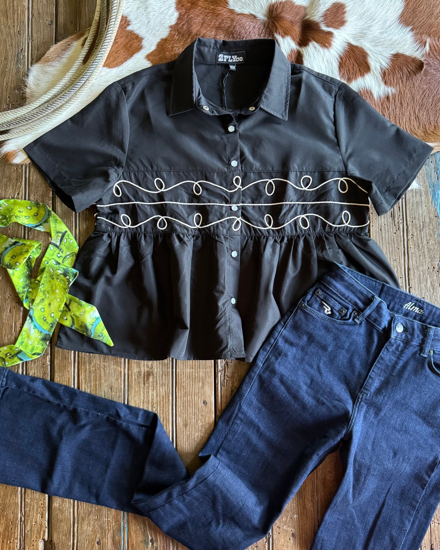 Black embroidered blouse and blue jeans on a wooden surface with cowhide rug in the background