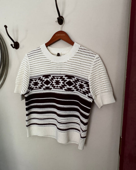 White sweater with black pattern on a wooden hanger against a neutral background