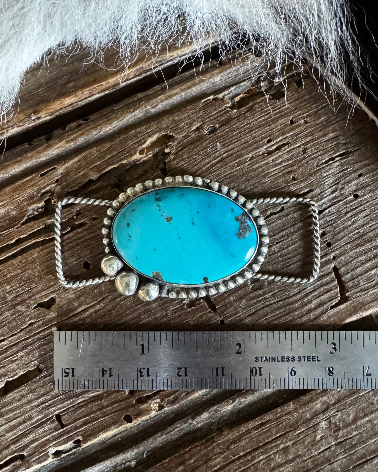 Turquoise pendant with silver frame and pearls on a wooden surface with a ruler for scale.