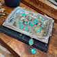 Turquoise and silver jewelry on a decorative tray with a wooden surface background