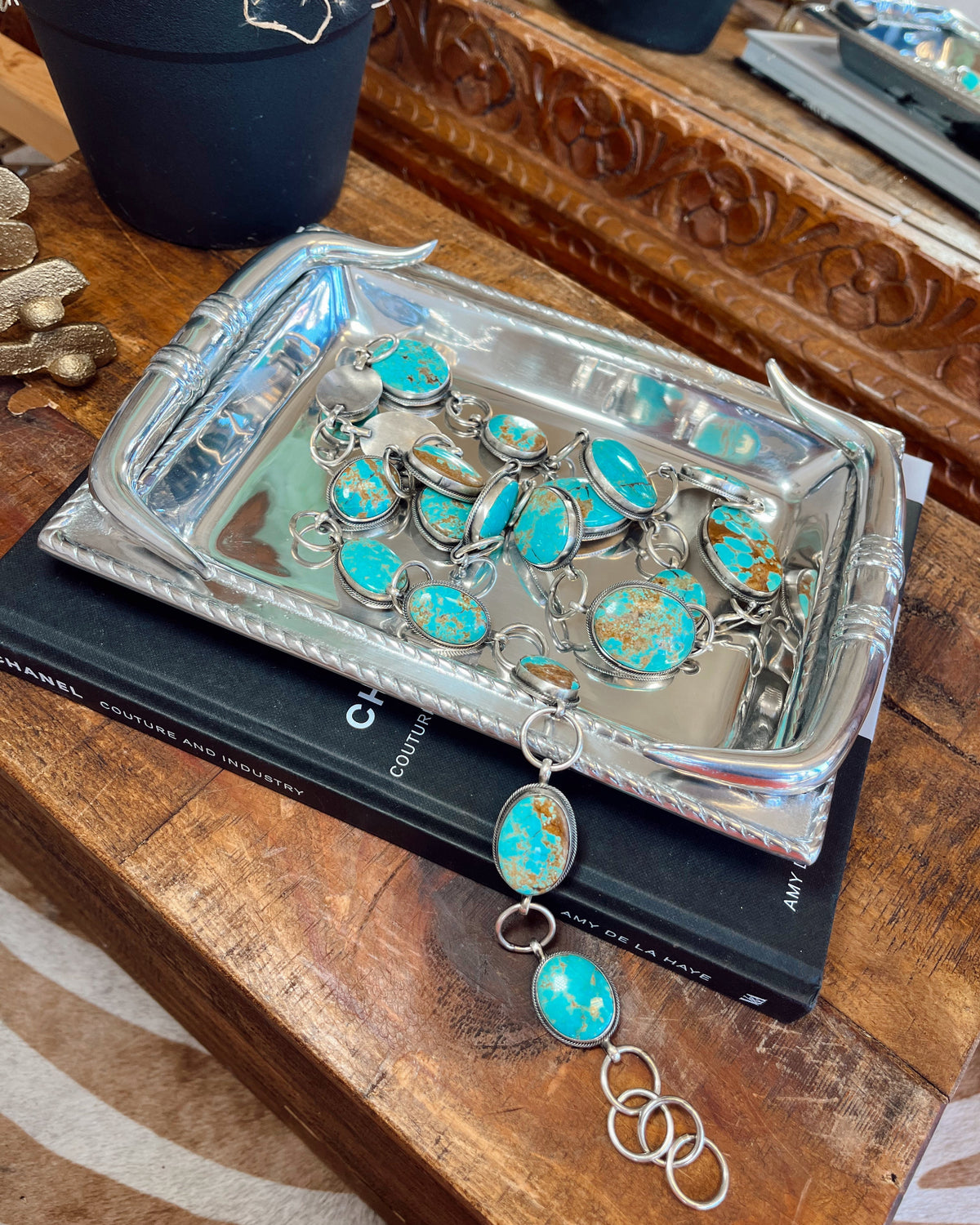 Turquoise and silver jewelry on a decorative tray with a wooden surface background