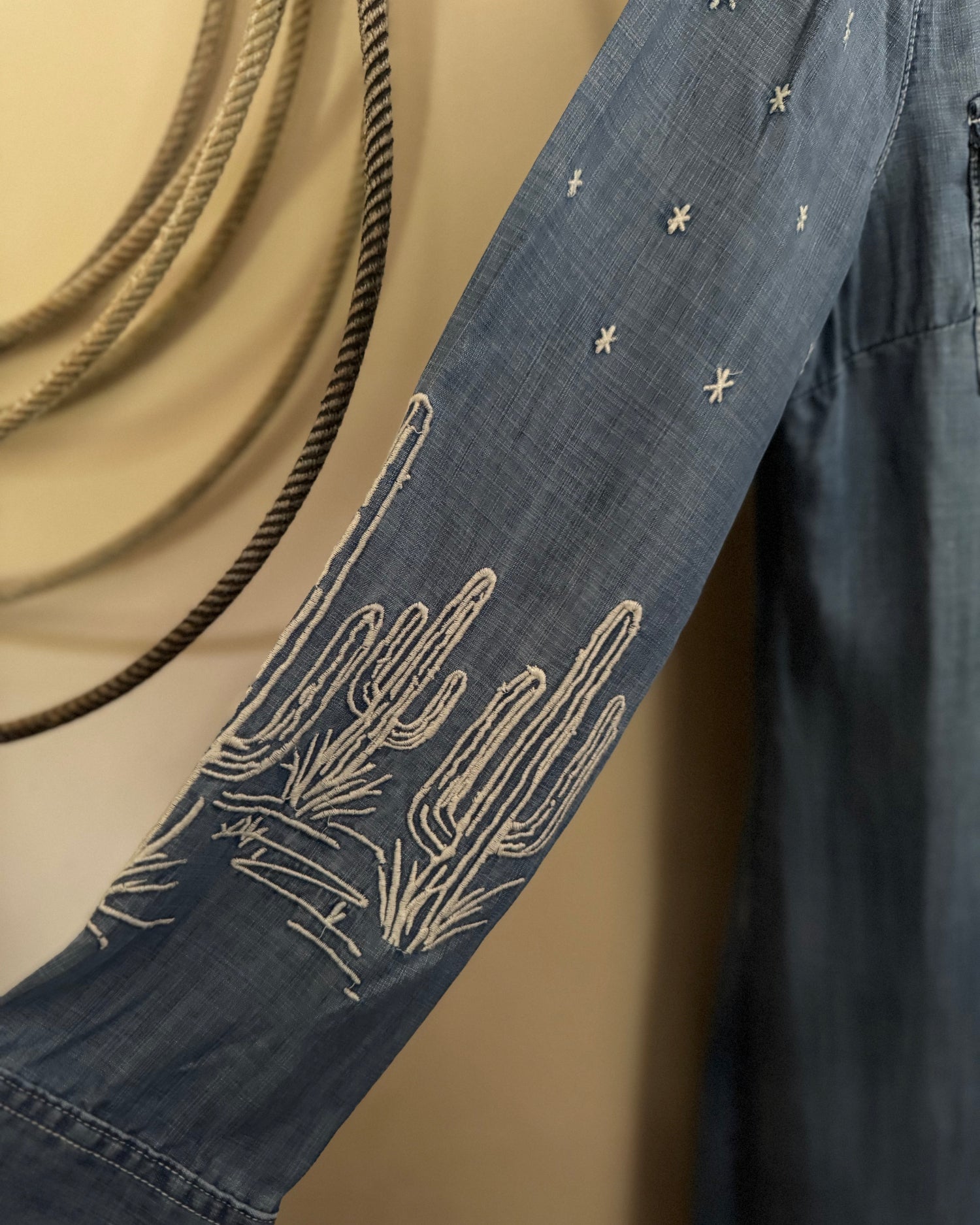 Blue denim shirt with white floral embroidery on a beige background