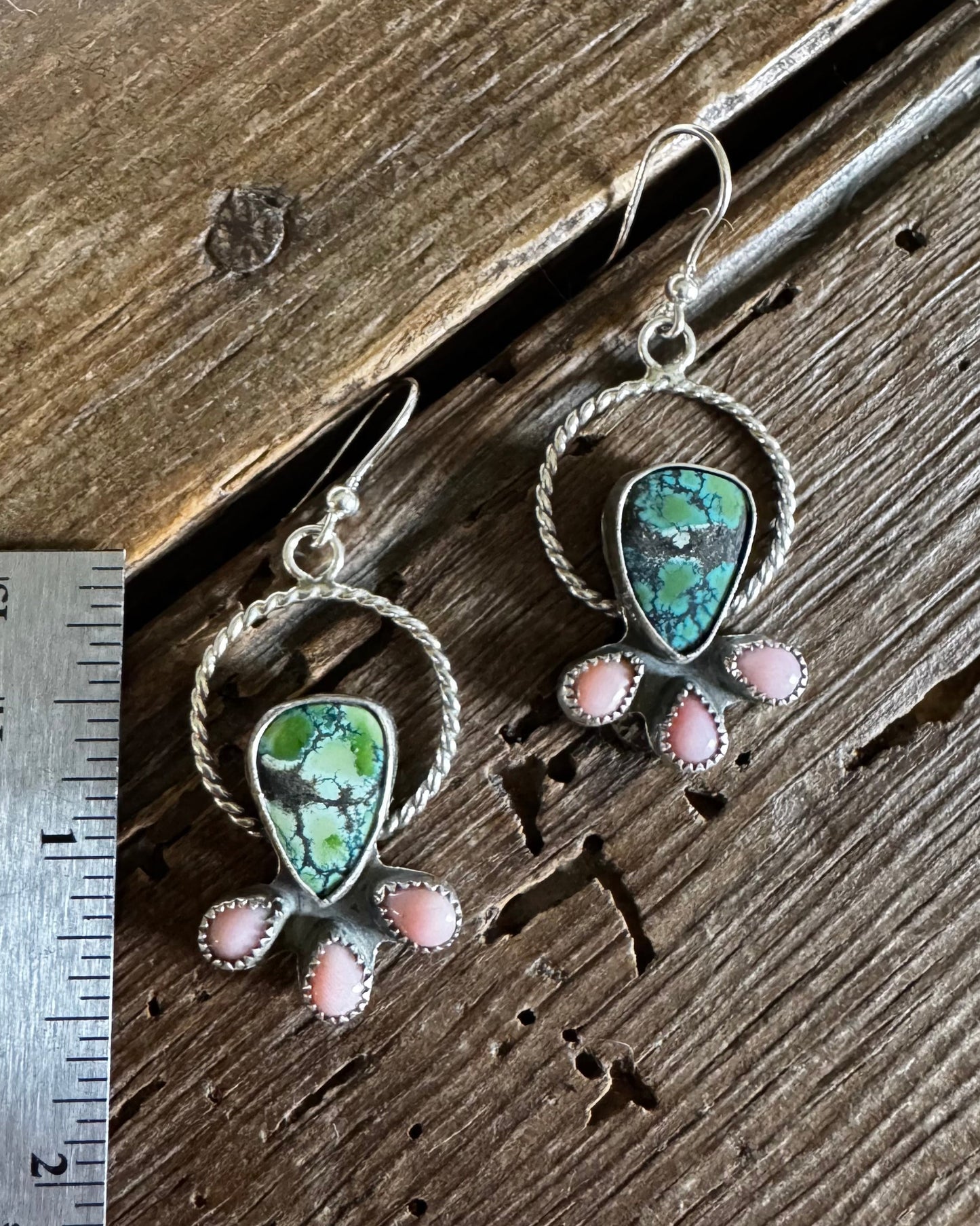 Pair of silver earrings with green and pink stones on a wooden surface with a ruler for scale.