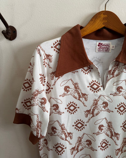 White shirt with brown pattern and collar on a wooden hanger against a white wall.