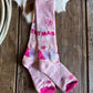 Pink Christmas-themed socks on a wooden surface with a cowhide rug in the background.