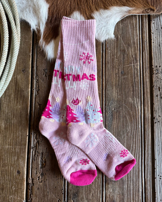 Pink Christmas-themed socks on a wooden surface with a cowhide rug in the background.