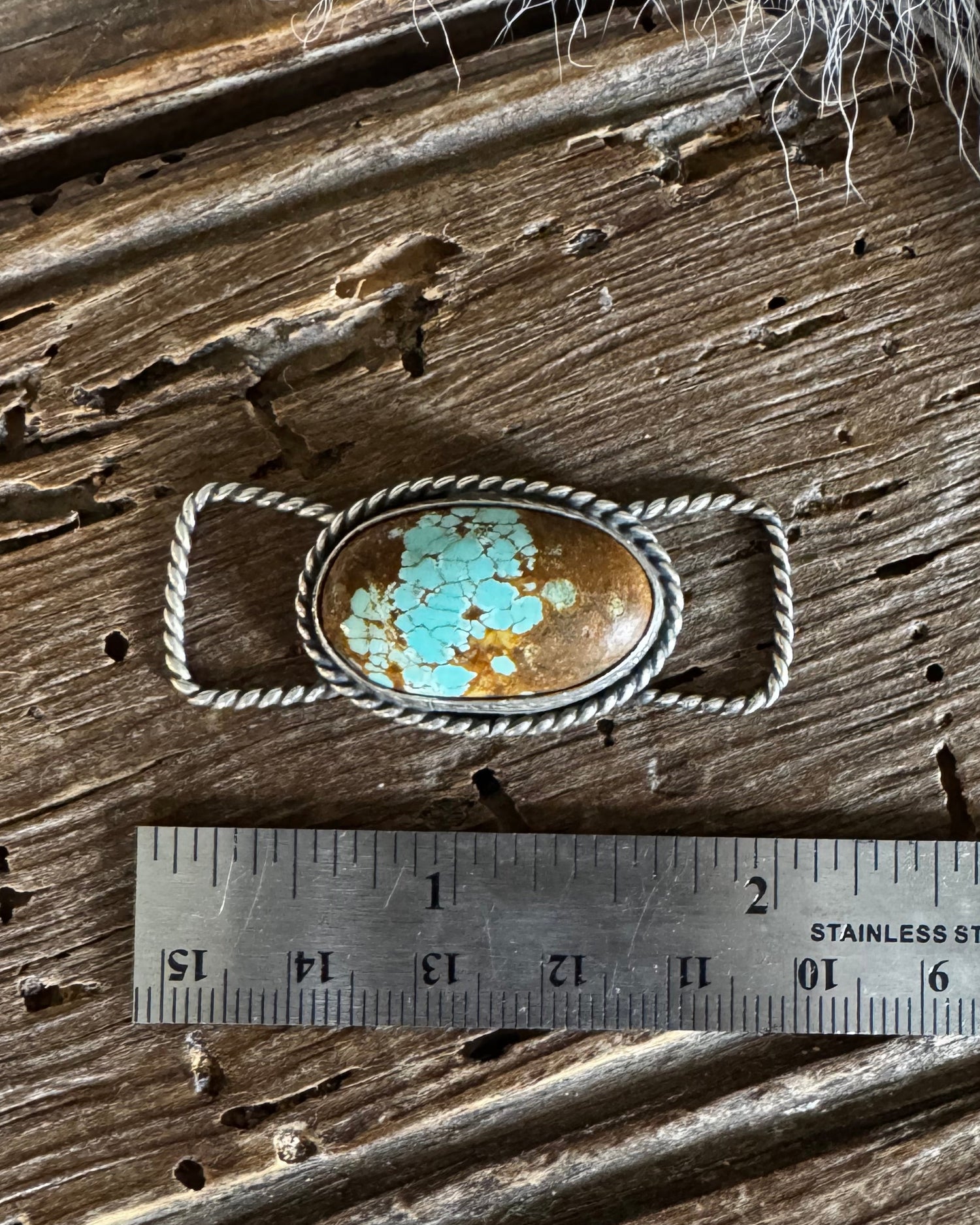 Silver twilly slide with a turquoise stone on a wooden surface with a ruler for scale.