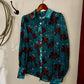 Blue shirt with red pattern hanging on a hook against a white wall.
