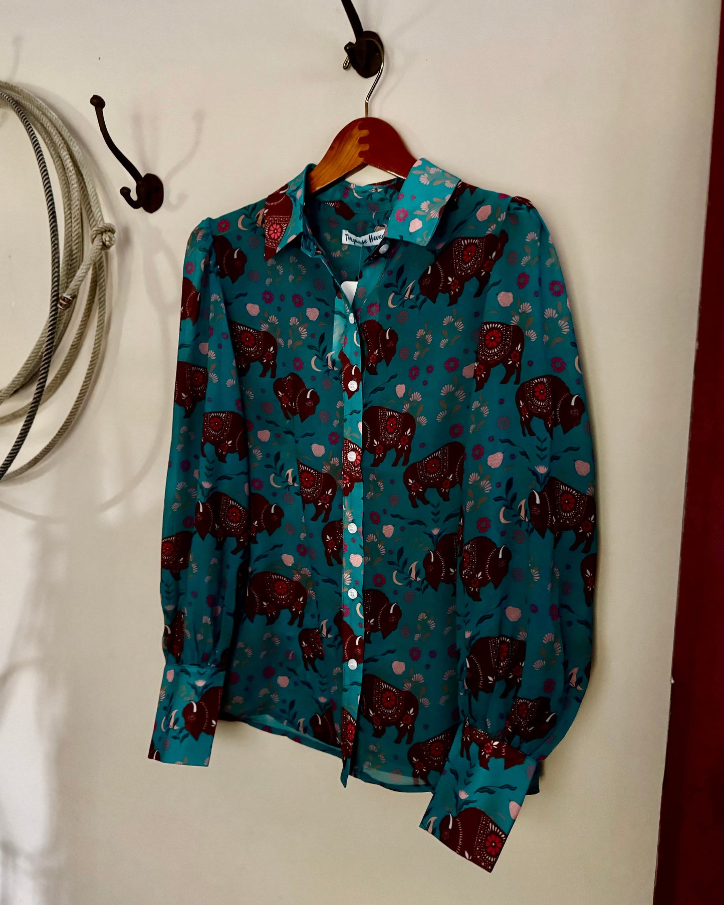Blue shirt with red pattern hanging on a hook against a white wall.