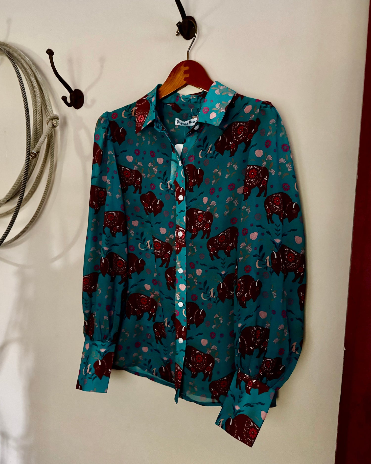 Blue shirt with red pattern hanging on a hook against a white wall.