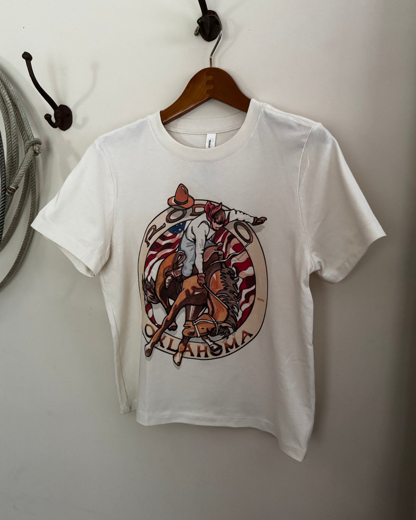 White t-shirt with a graphic design of a horse and text, hanging on a wooden hanger against a plain wall.