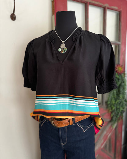 Black blouse with colorful stripes on a mannequin against a neutral wall.