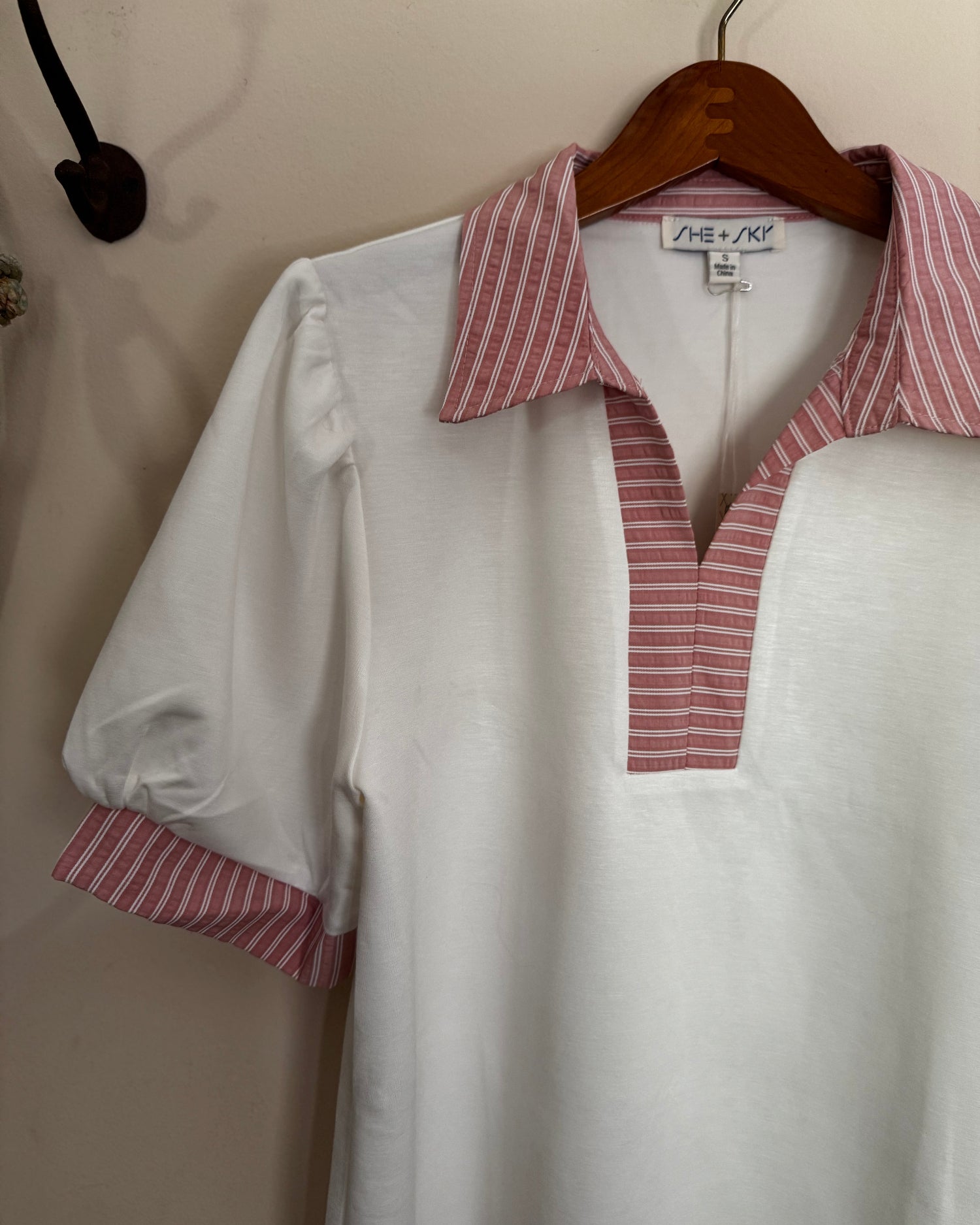 White blouse with red and white striped collar and cuffs on a hanger.