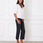 Woman wearing a white blouse and dark pants against a white wall.
