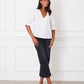 Woman wearing a white blouse and black pants against a white wall.