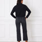 Person wearing a black shirt and dark jeans standing against a white paneled wall.