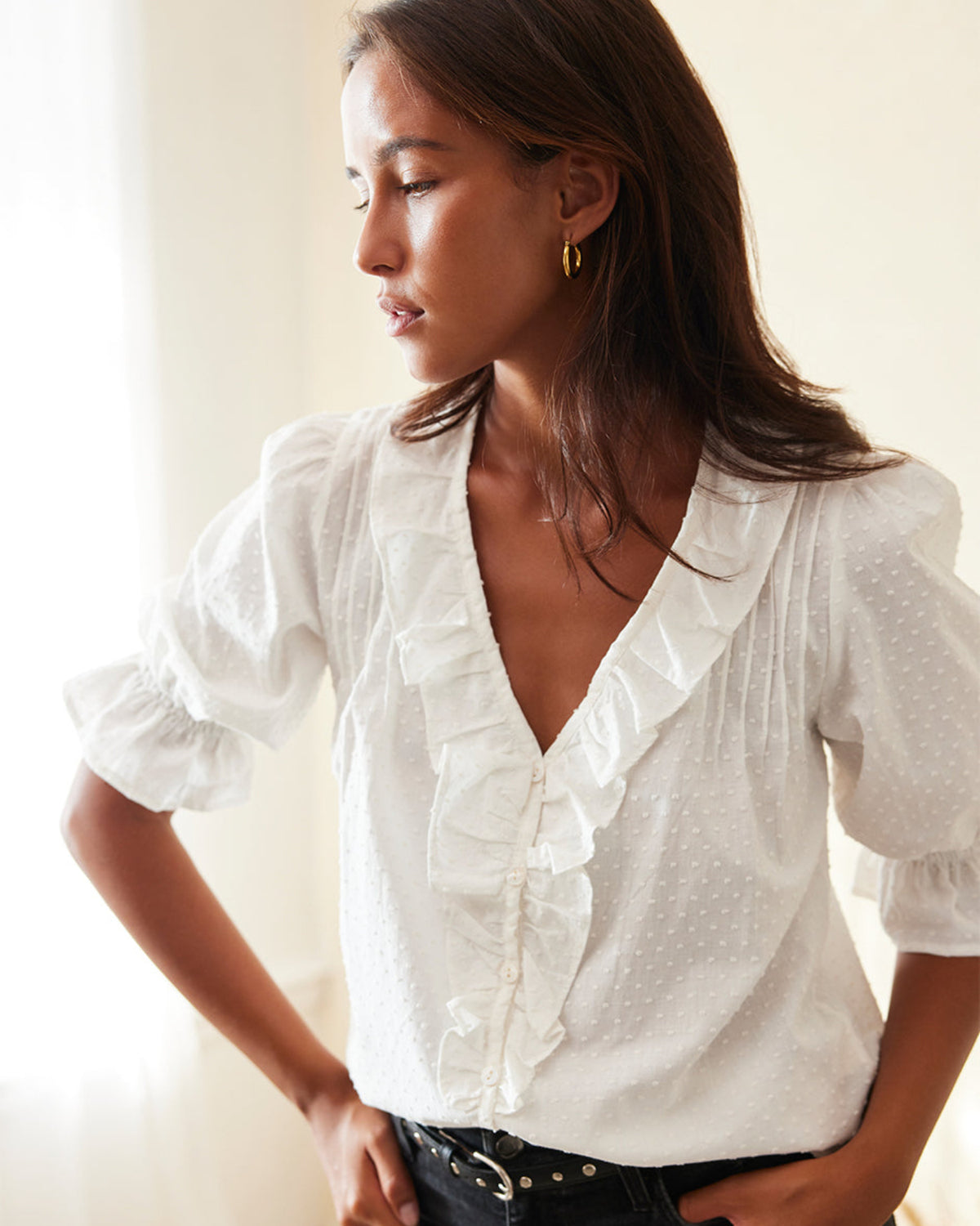 Woman wearing a white blouse with ruffled sleeves against a neutral background