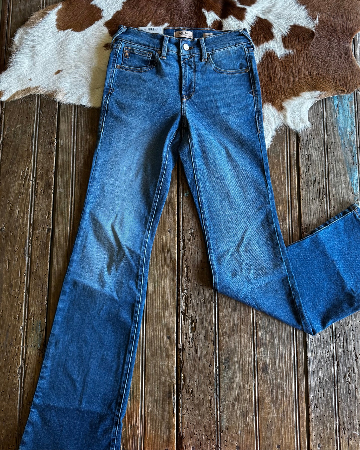 Blue jeans on a wooden floor with a cowhide rug in the background