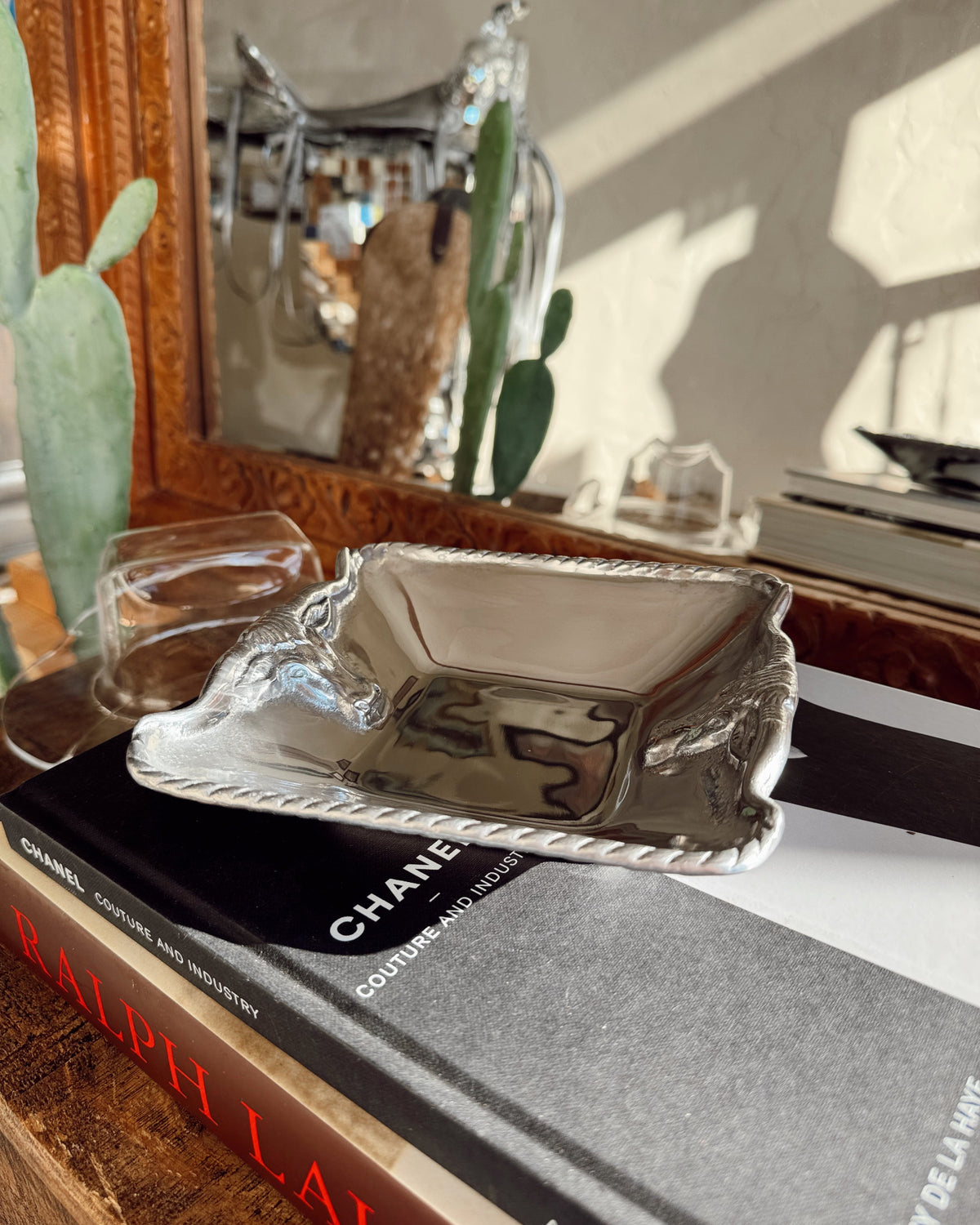 Silver dish on top of a Chanel book with a mirror and cacti in the background