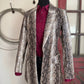 Patterned coat with a red shirt underneath on a mannequin against a neutral wall.